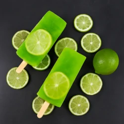 Green lime popsicles with lime slices, surrounded by fresh lime on a dark surface.